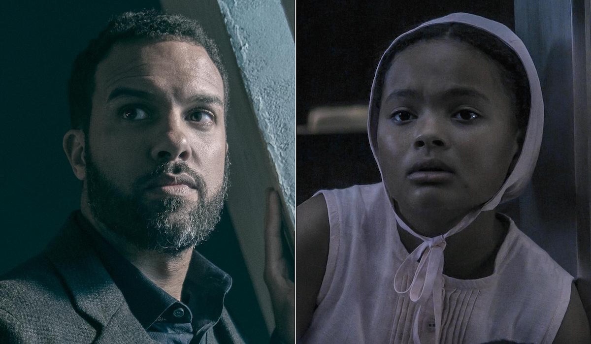 O-T Fagbenle as Luke (L) and Jordana Blake as Hannah (R) in 'The Handmaid's Tale' Season 4. He wears a sweater and tweed suit and stands near a window. She wears a pink dress and pink bonnet while holding a doll in a large glass cell.