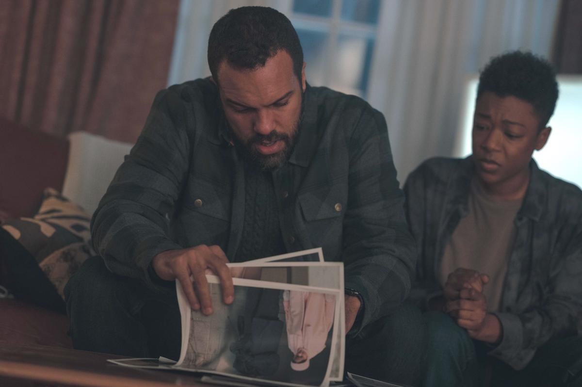 O-T Fagbenle wears a blue and green flannel while looking through pictures as Luke and Samira Wiley wears a similarly colored flannel as Moira in 'The Handmaid's Tale' Season 4. They have eager and concerned looks on their faces and sit on a couch.