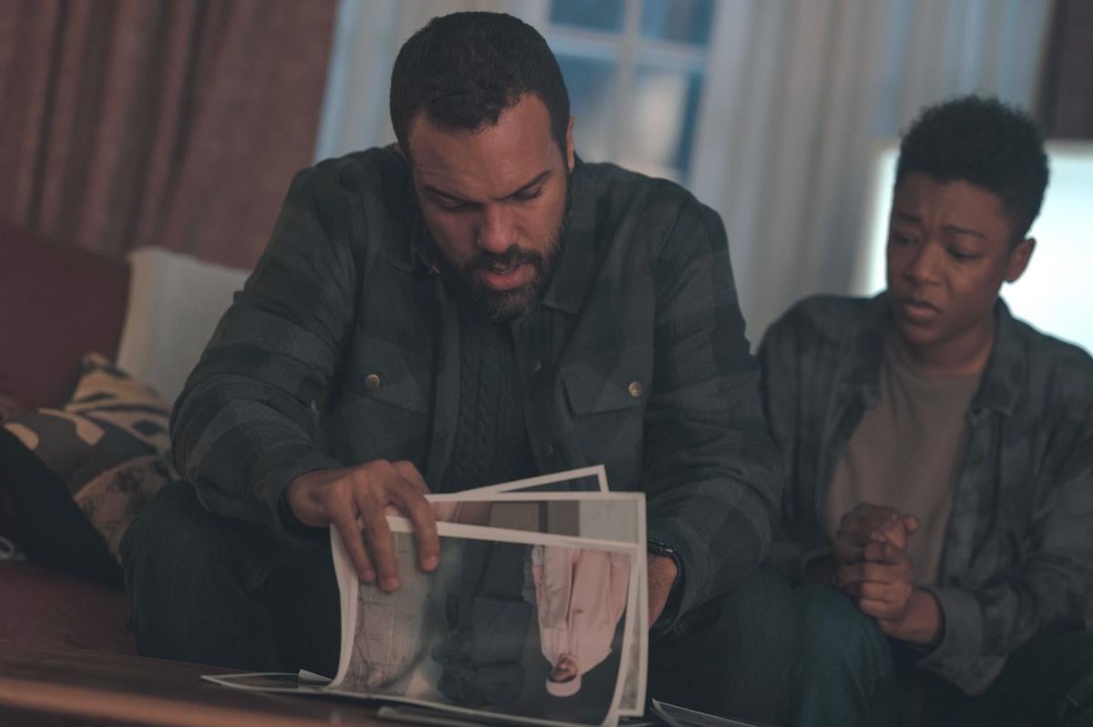 O-T Fagbenle wears a blue and green flannel while looking through pictures as Luke and Samira Wiley wears a similarly colored flannel as Moira in 'The Handmaid's Tale' Season 4. They have eager and concerned looks on their faces and sit on a couch.
