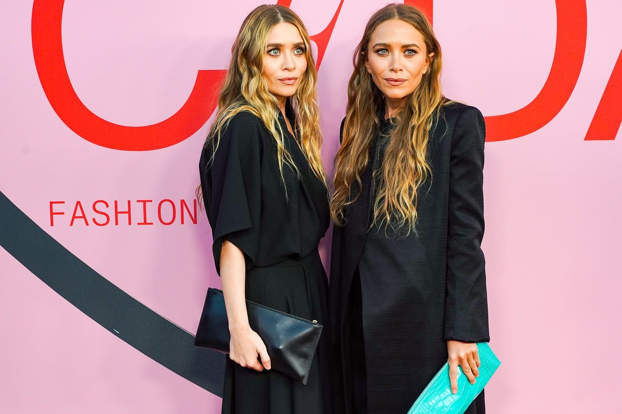 Mary-Kate Olsen and Ashley Olsen don all black in front of pink backdrop