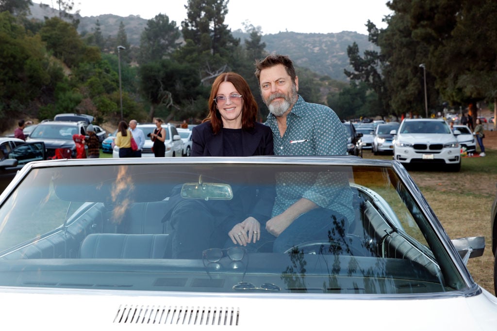Megan Mullally and Nick Offerman sit on top of their convertible's seats as they prepare to watch a drive-in movie. Offerman has his are around Mullally and they're all smiles.
