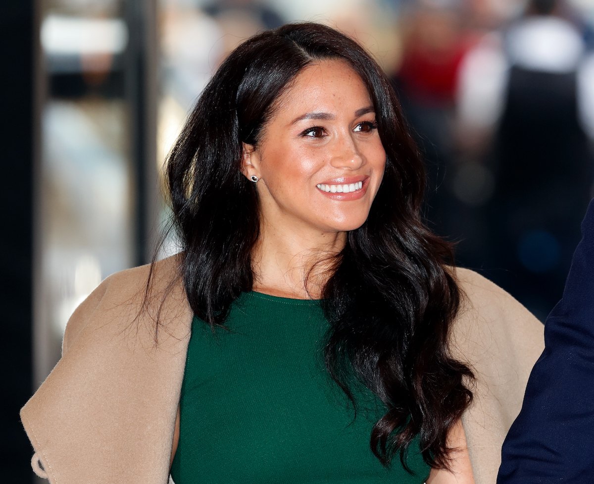 Meghan, Duchess of Sussex grins in a green dress and beige coat