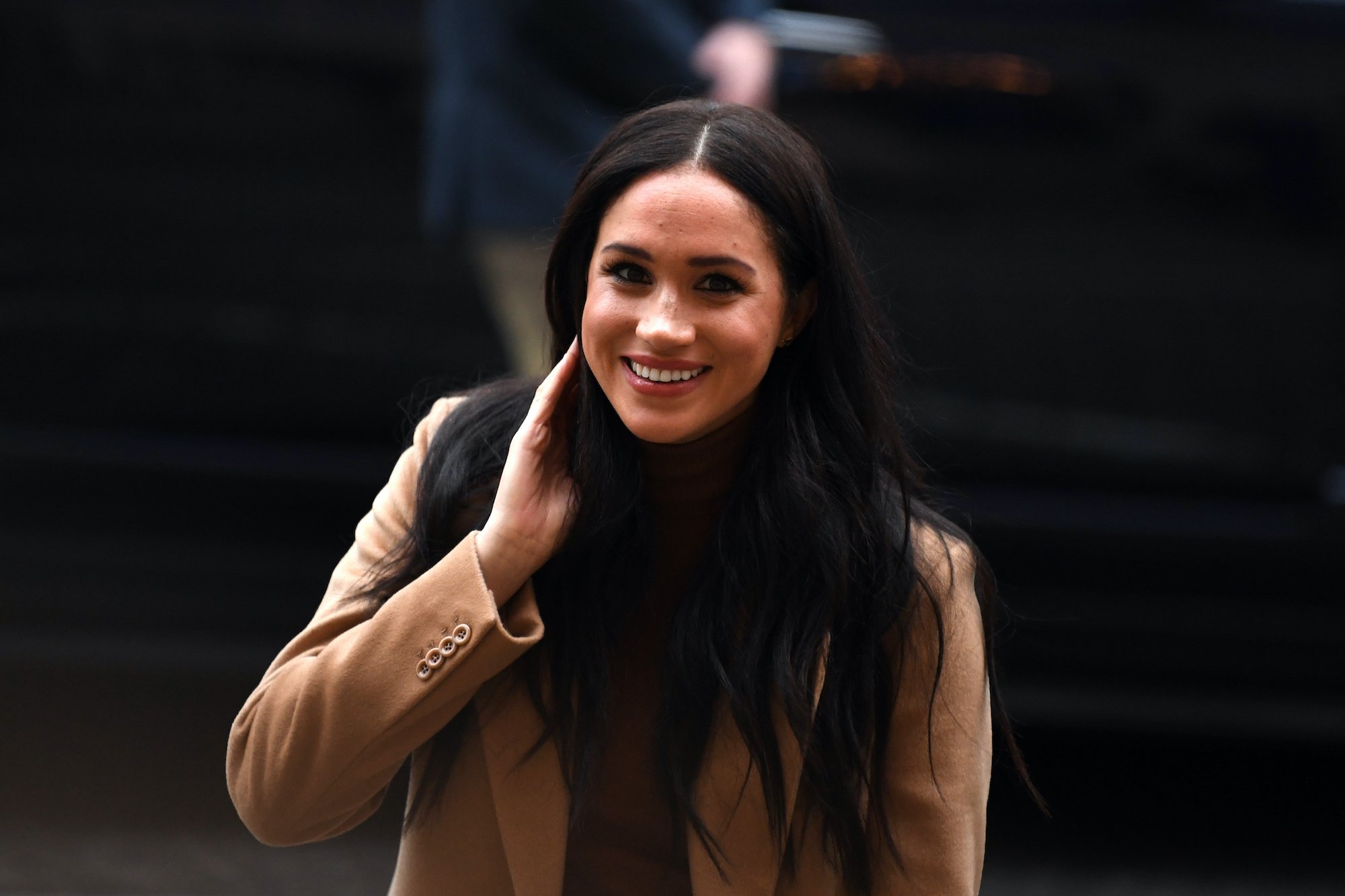 Meghan Markle smiling, tucking her hair back