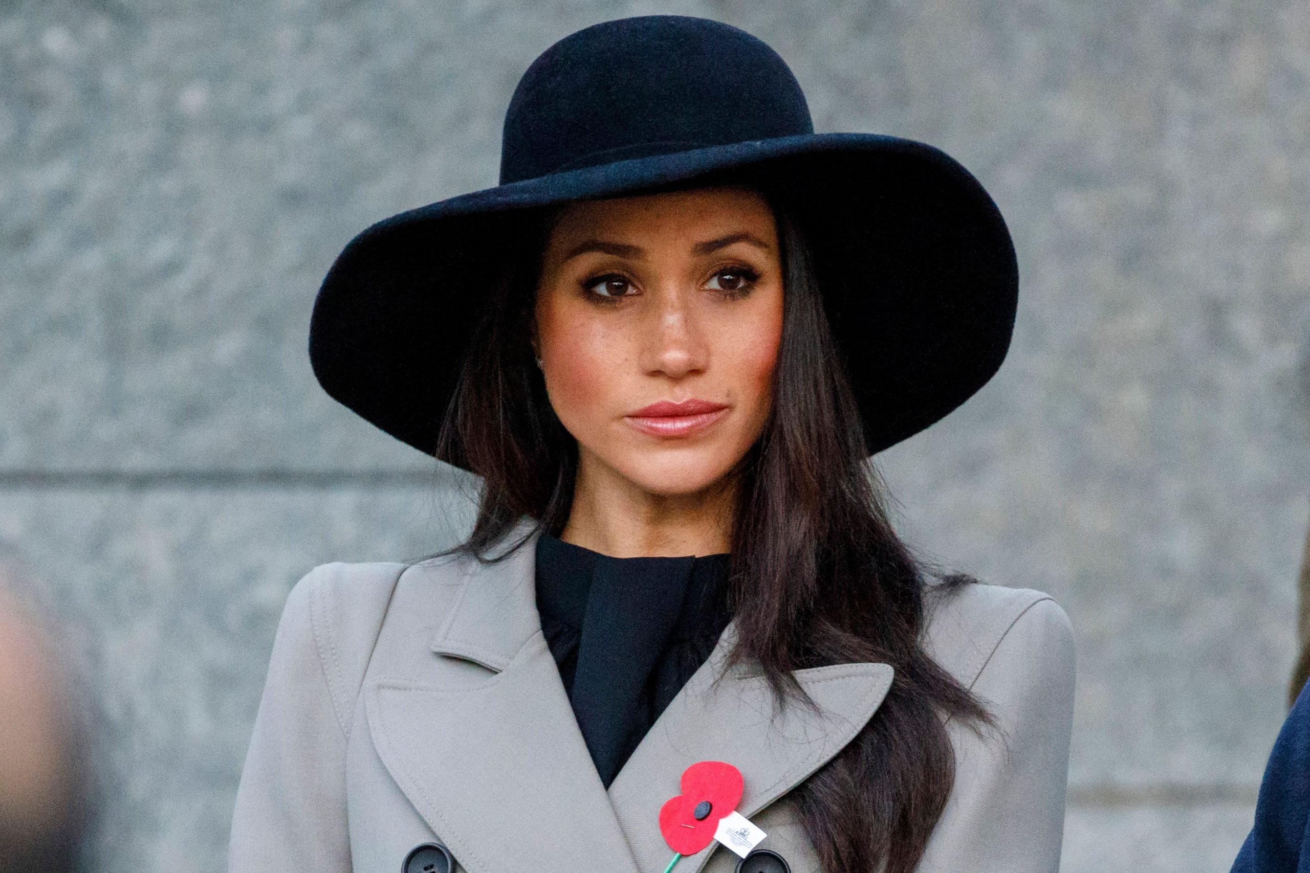 Meghan Markle looks on wearing a gray coat and black hat