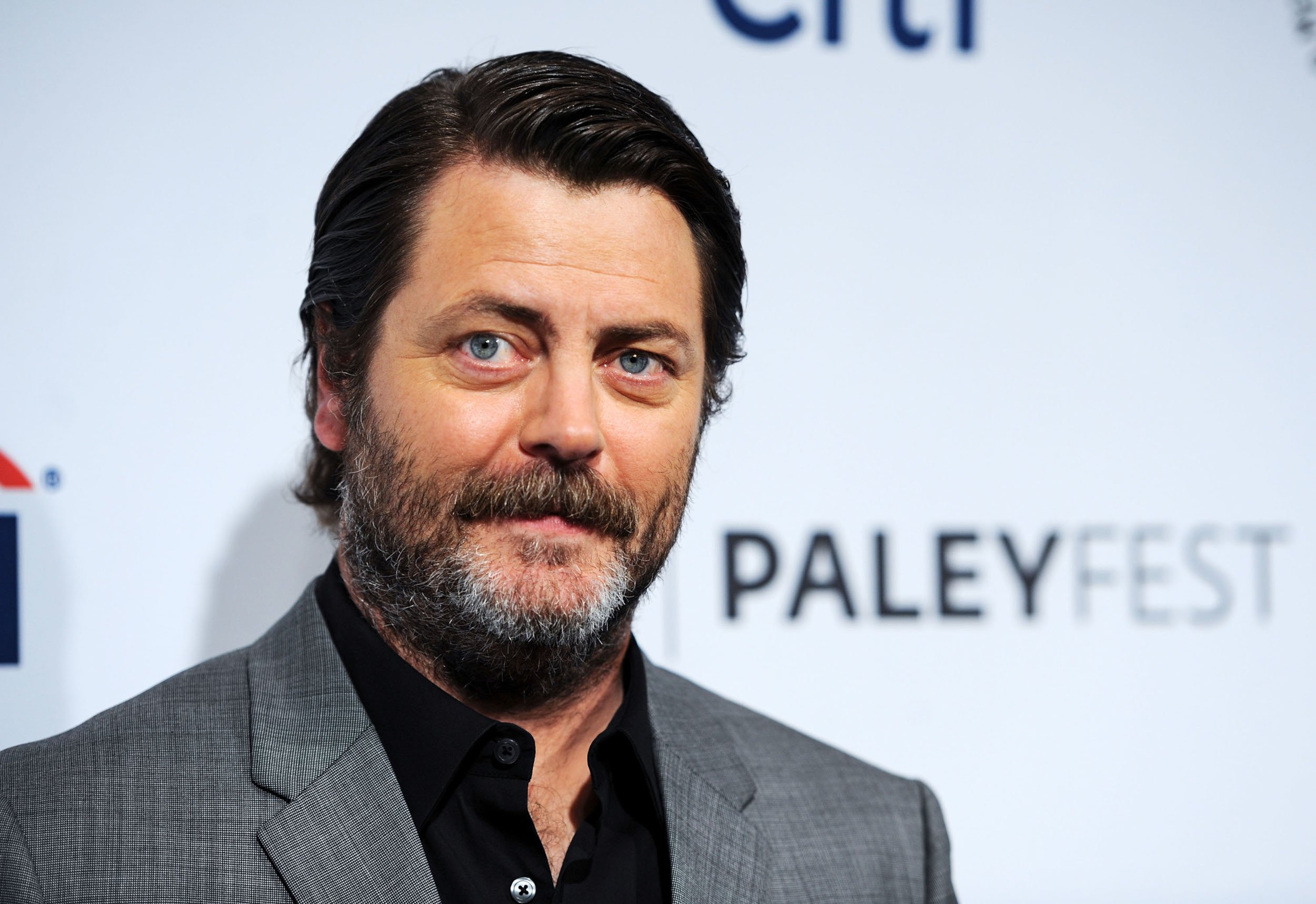 'Parks and Recreation' star Nick Offerman wearing a grey suit and standing in front of a PaleyFest wall