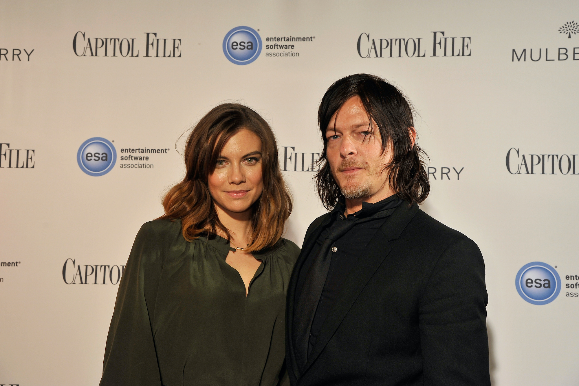 Lauren Cohan and Norman Reedus smiling in front of a white background