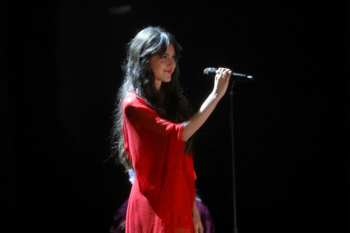 Olivia Rodrigo holding a microphone in a red dress