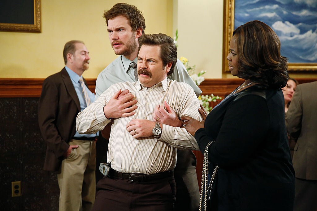 Chris Pratt as Andy Dwyer and Retta as Donna Meagle hold back Nick Offerman as Ron Swanson as he falls back with disgust.