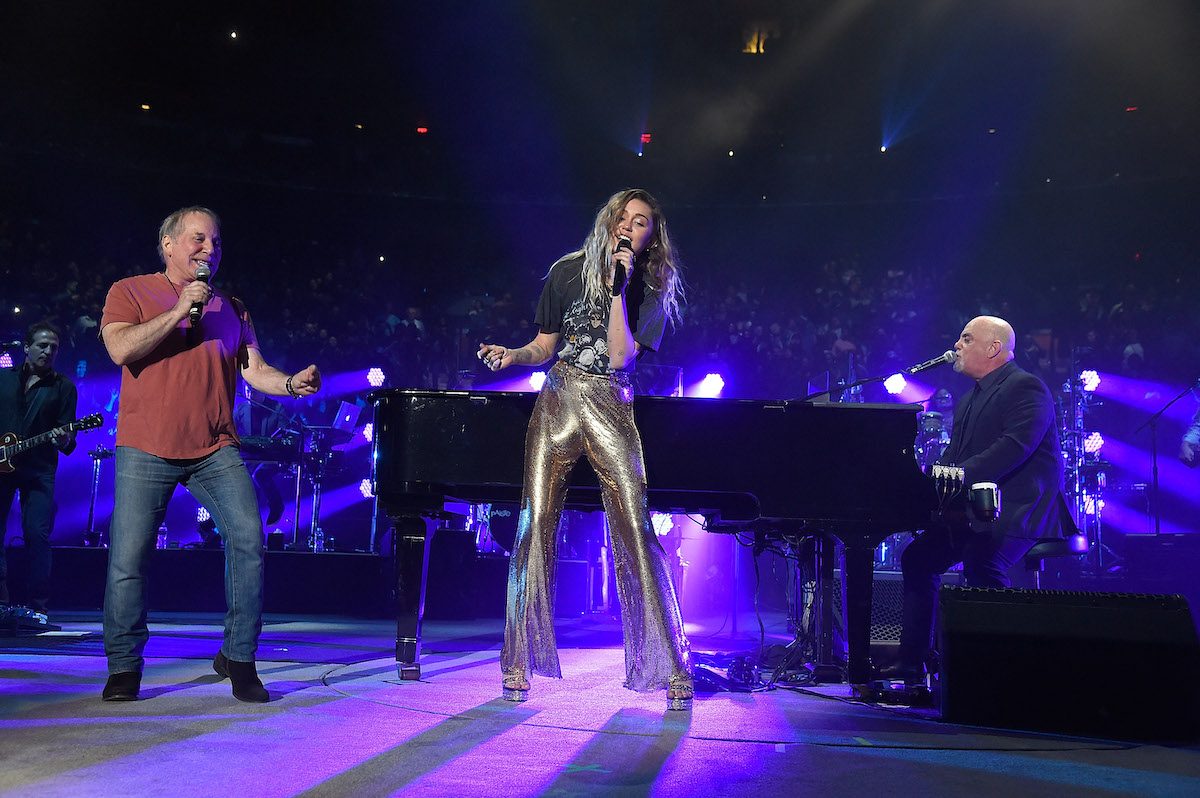 Paul Simon and Miley Cyrus sing as they stand near Billy Joel at the piano while performing at Madison Square Garden in 2017
