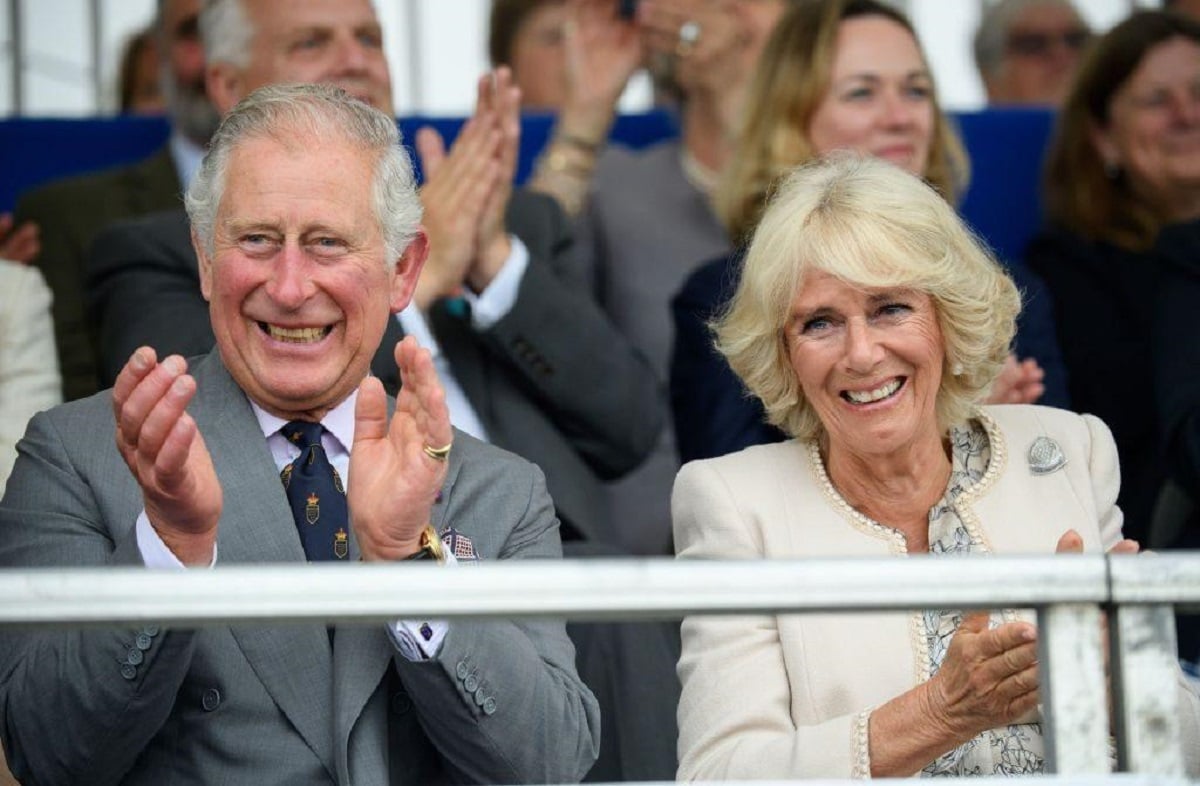 Prince Charles and Camilla Parker Bowles seated next to each other cheering at an event