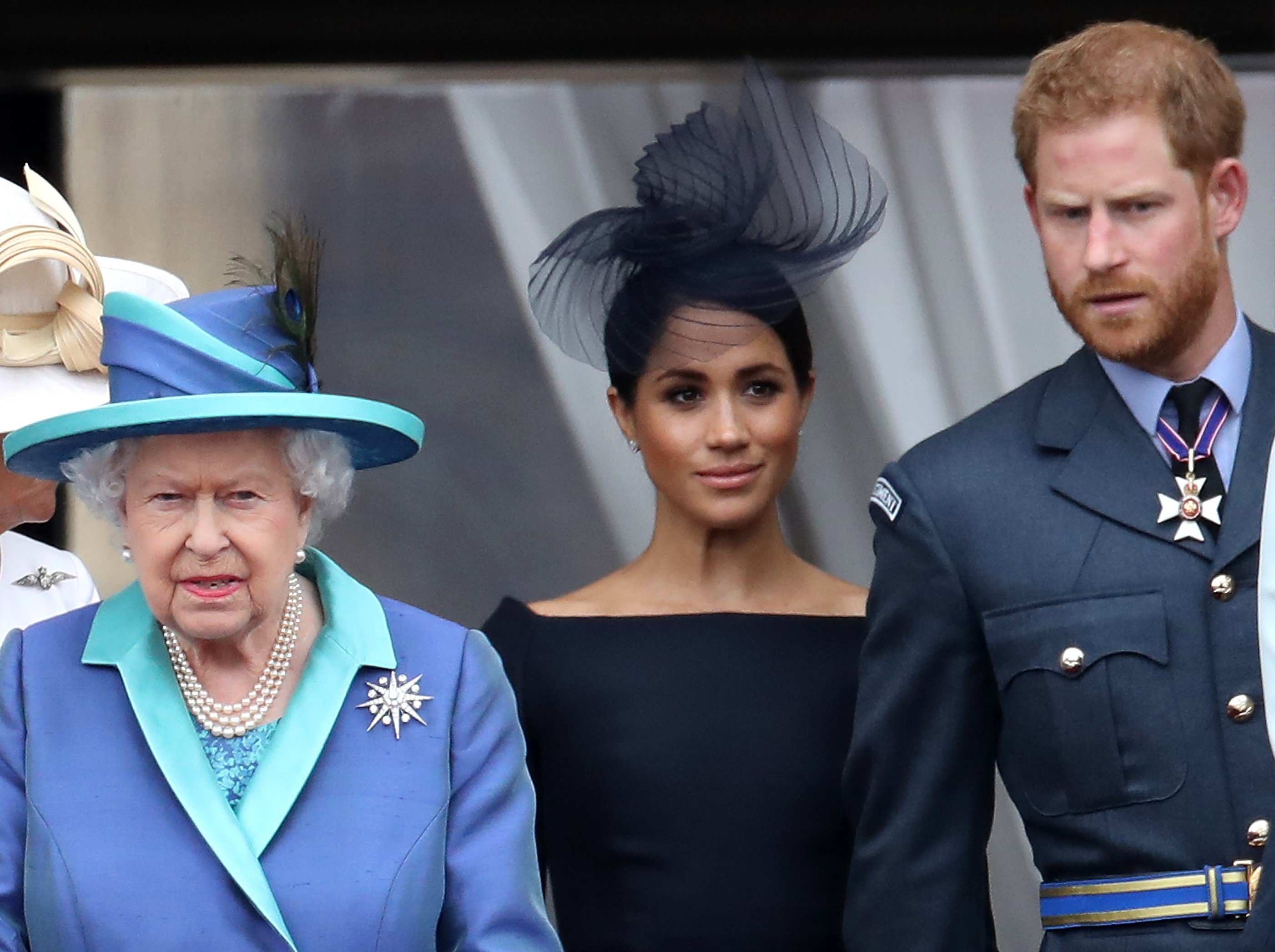 Queen Elizabeth II, Prince Harry, and Meghan Markle standing on the balcony of Buckingham Palace to mark the Centenary of the RAF