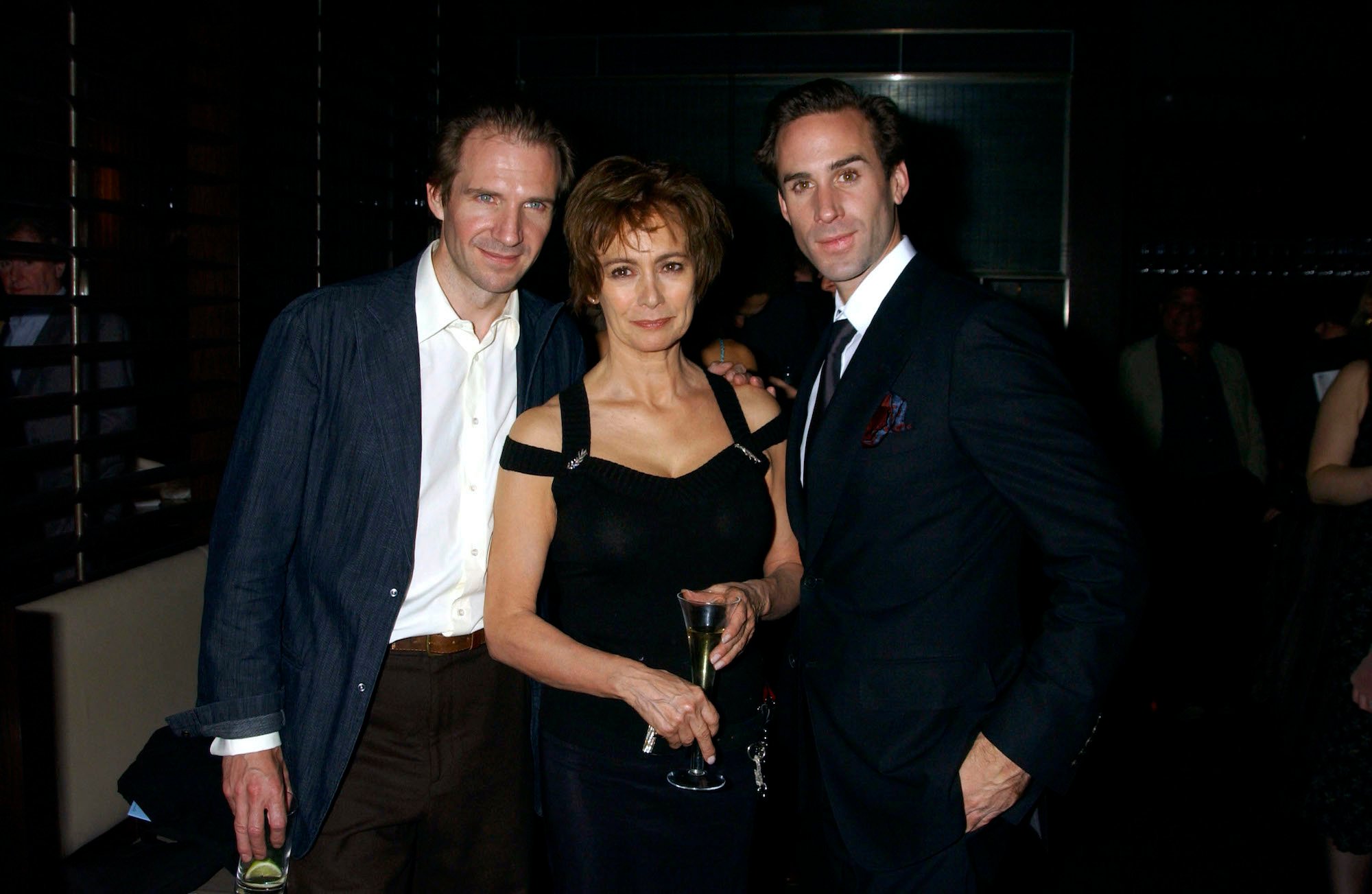 Ralph Fiennes, Francesca Annis, and Joseph Fiennes smiling in front of a dark background