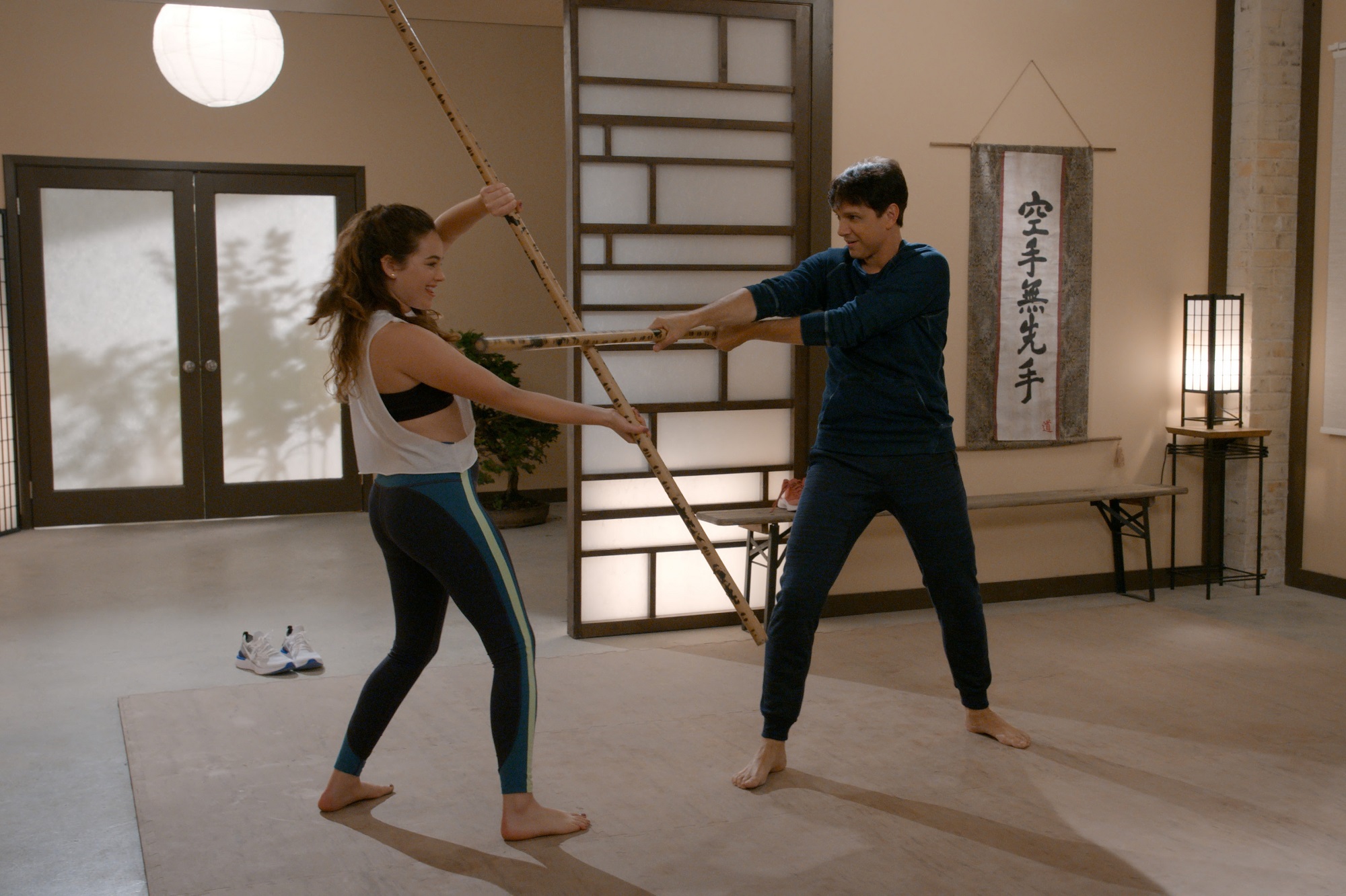 Ralph Macchio and Mary Mouser spar with staffs
