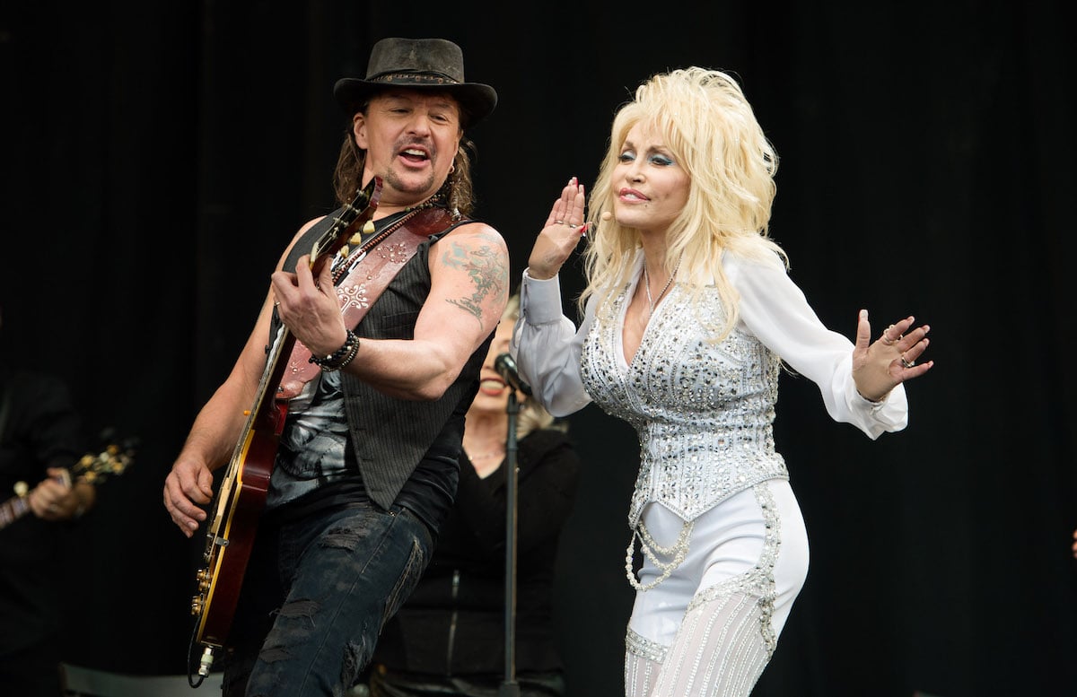 Dolly Parton sings in a white outfit with Richie Sambora of Bon Jovi playing guitar next to her on stage.