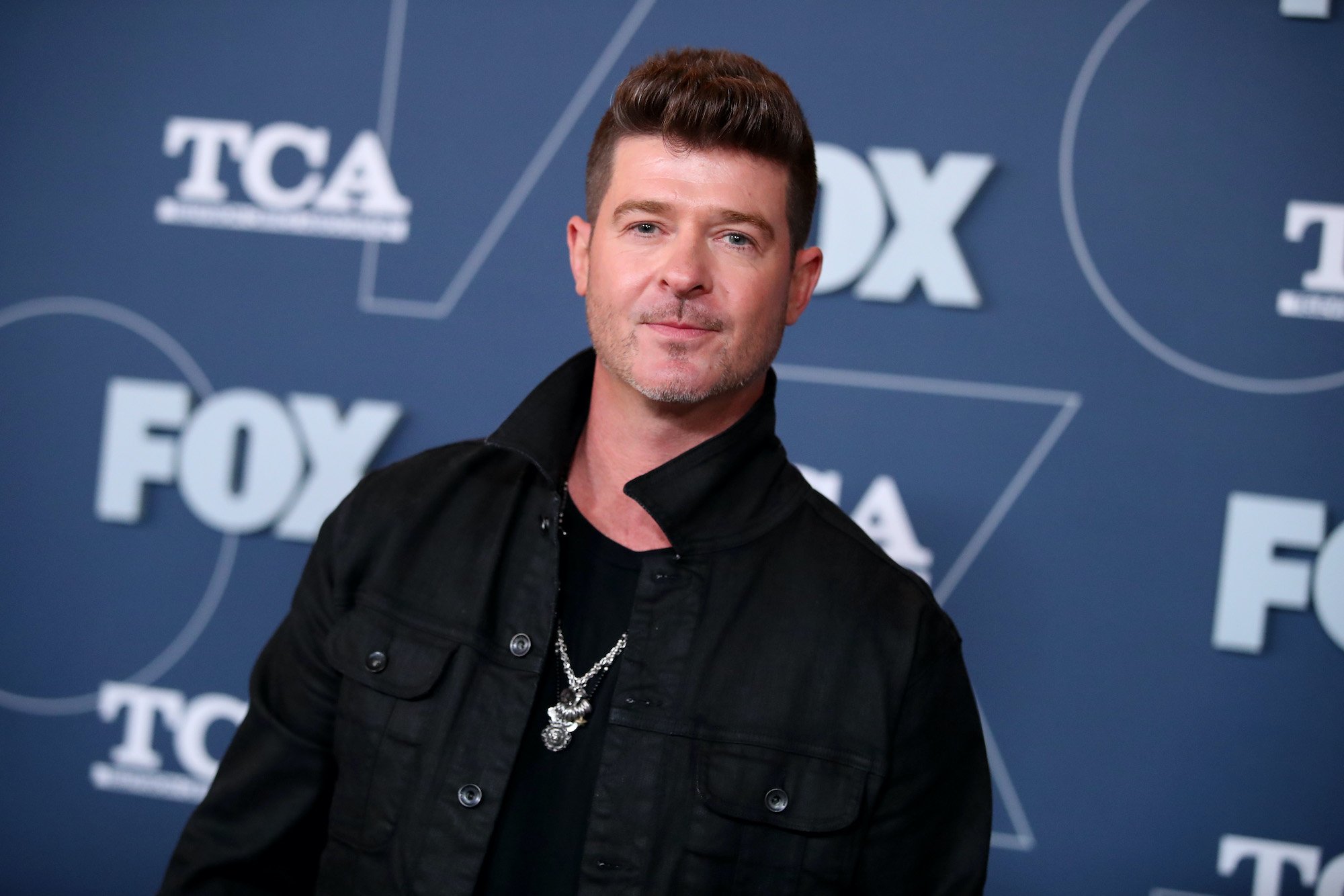Robin Thicke smiling in front of a blue background