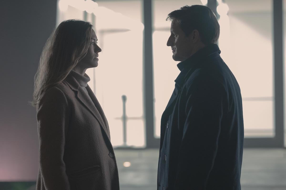 Yvonne Strahovski wearing a cream turtleneck and pink coat as Serena Joy and Sam Jaeger wearing a dark peacoat as Mark Tuello in 'The Handmaid's Tale' Season 4. They stand outside at night and look at each other with serious faces.