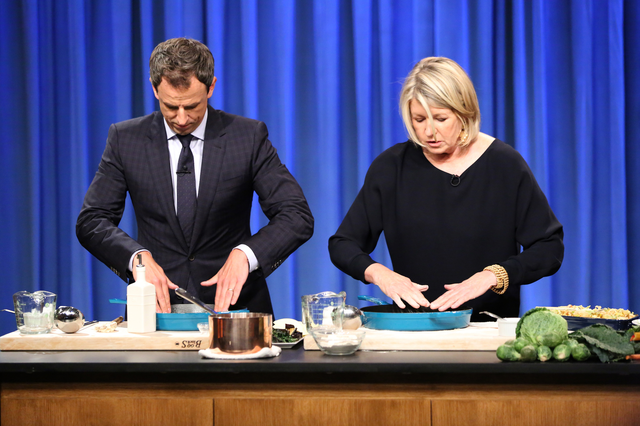 Seth Meyers cooking Martha Stewart's recipes next to her against a blue background for a late-night television program