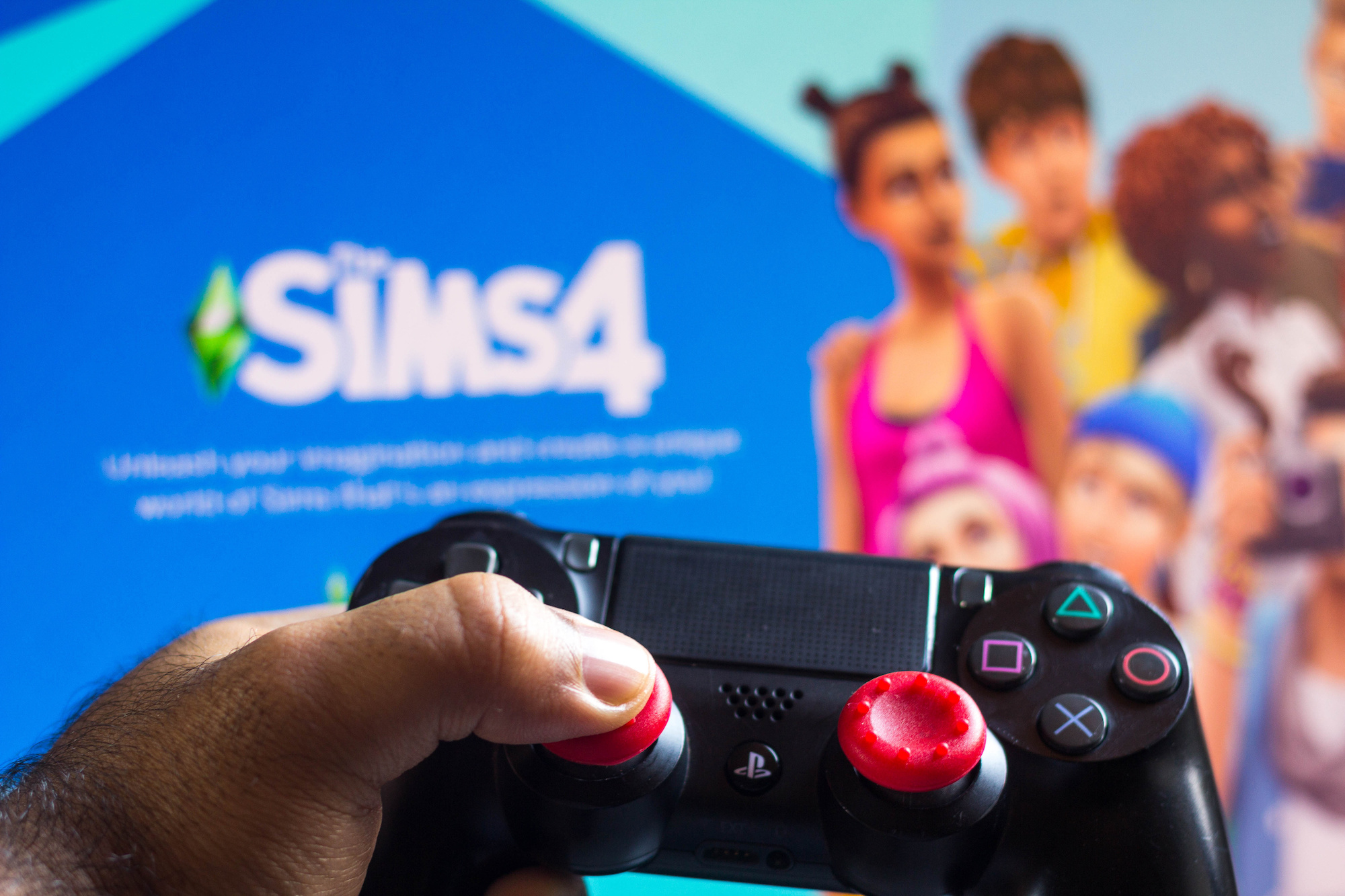 PlayStation (PS) controller and The Sims 4 game logo seen in he background