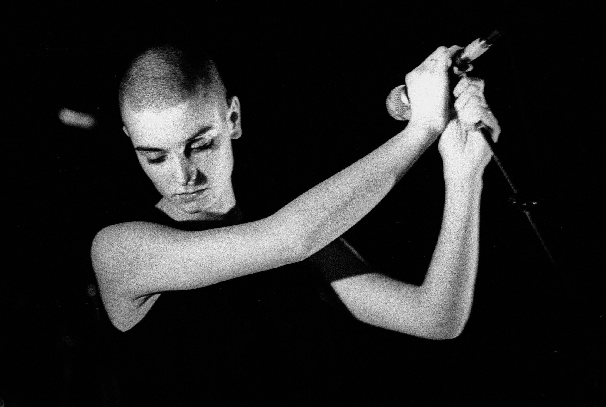 Sinead O'Connor looking down, holding a microphone, in black and white