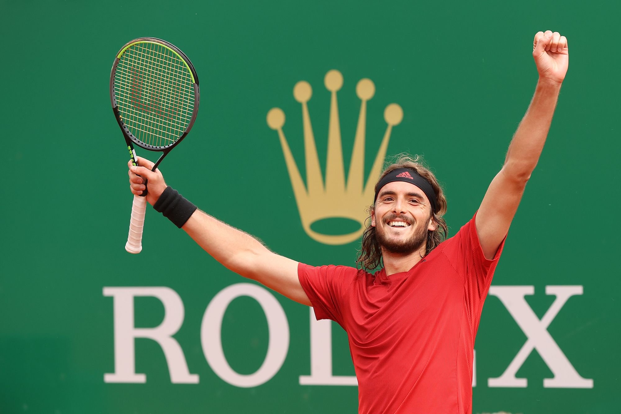 Stefanos Tsitsipas smiling, holding his arms up in a victorious pose