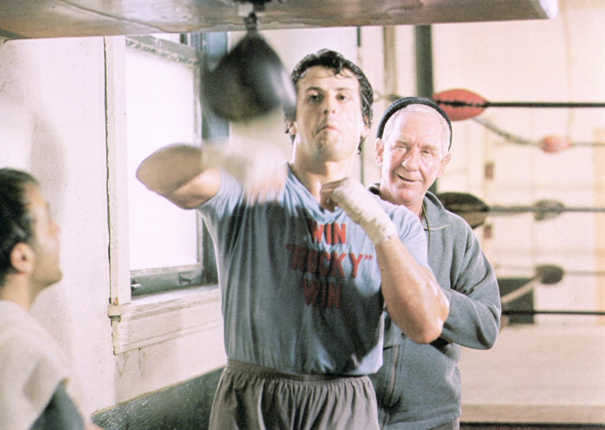 Sylvester Stallone hits a punching bag as Rocky Balboa while Burgess Meredith as Mickey stands behind him in a scene from 'Rocky'