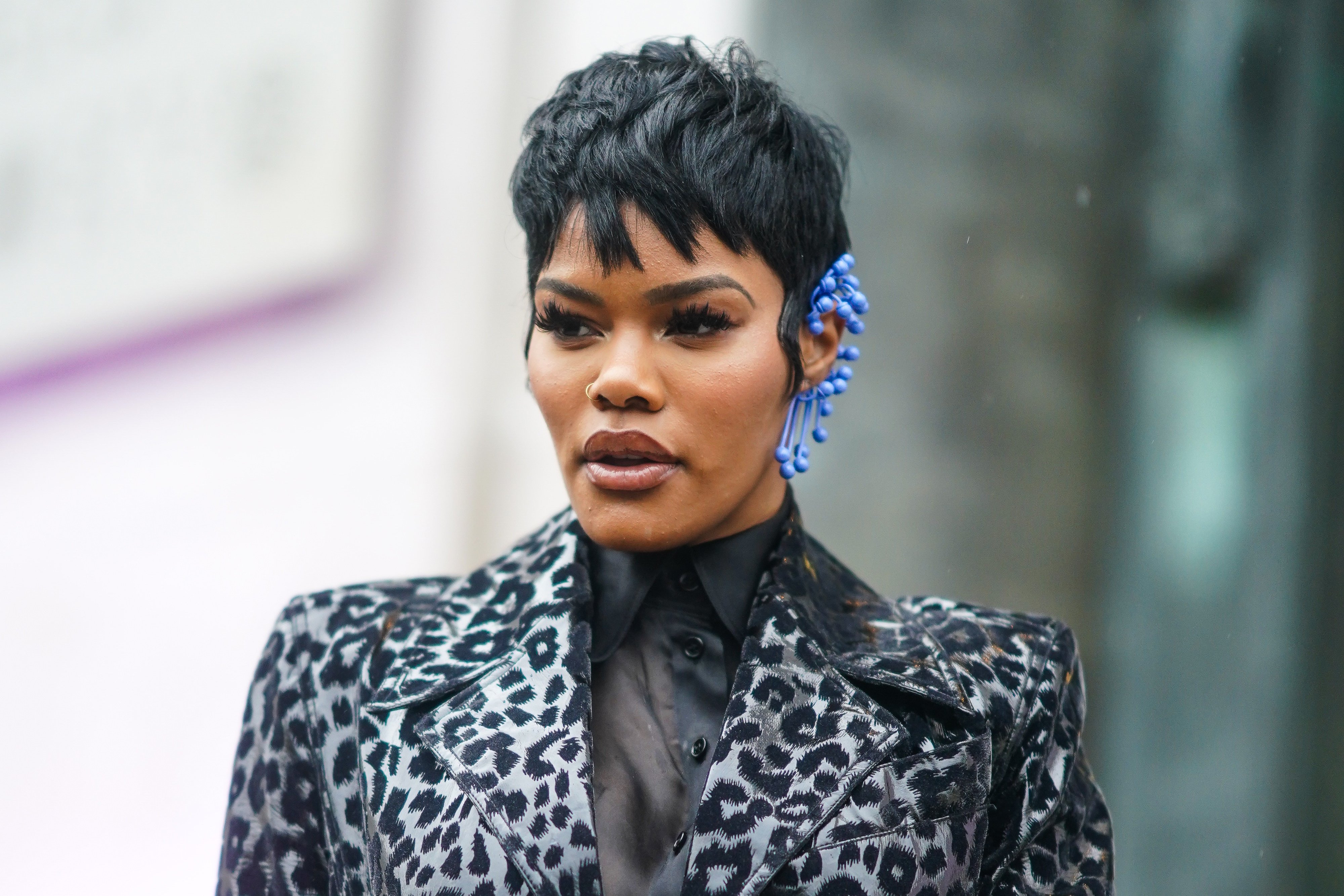 Teyana Taylor wears a black shirt, a black and gray leopard print long trench coat, a blue earring, outside Mugler, during Paris Fashion Week - Womenswear Fall/Winter 2020/2021