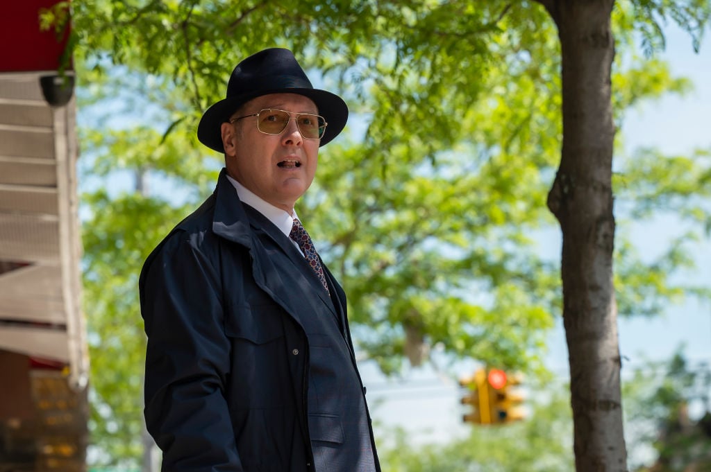 James Spader as Raymond 'Red' Reddington stands outside with a hat and jacket, looking into the distance.