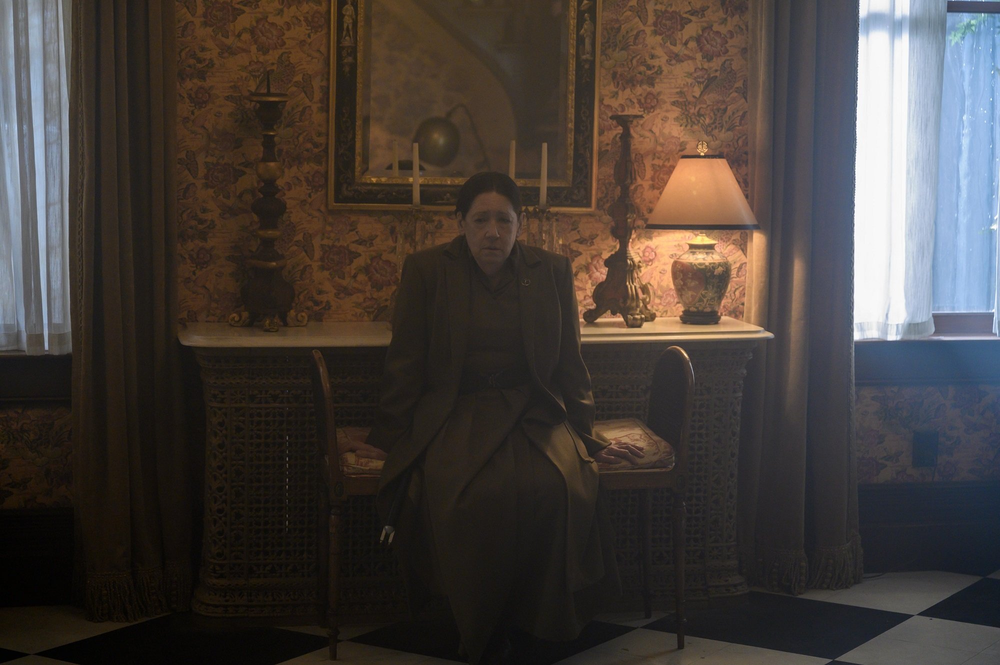 Aunt Lydia sits on a padded bench in a dimly-lit room in 'The Handmaid's Tale'