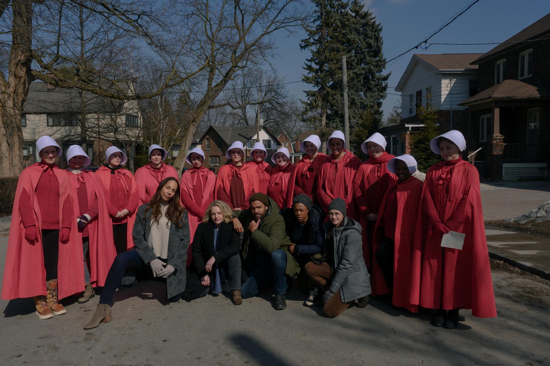 Handmaids and actors all standing together and smiling at the camera while on the set of 'The Handmaid's Tale' Season 4