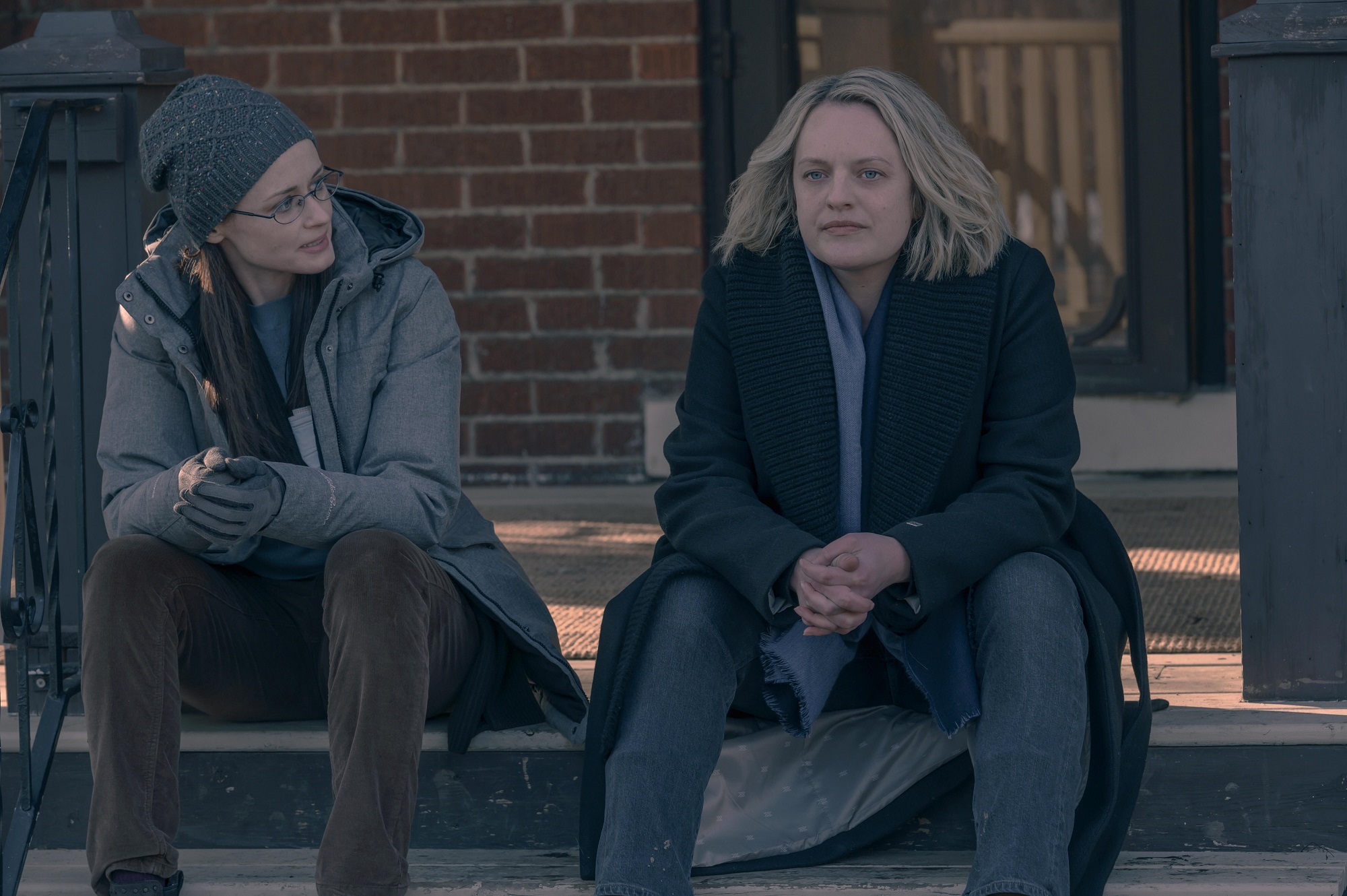 Emily and June sit on porch steps in 'The Handmaid's Tale'