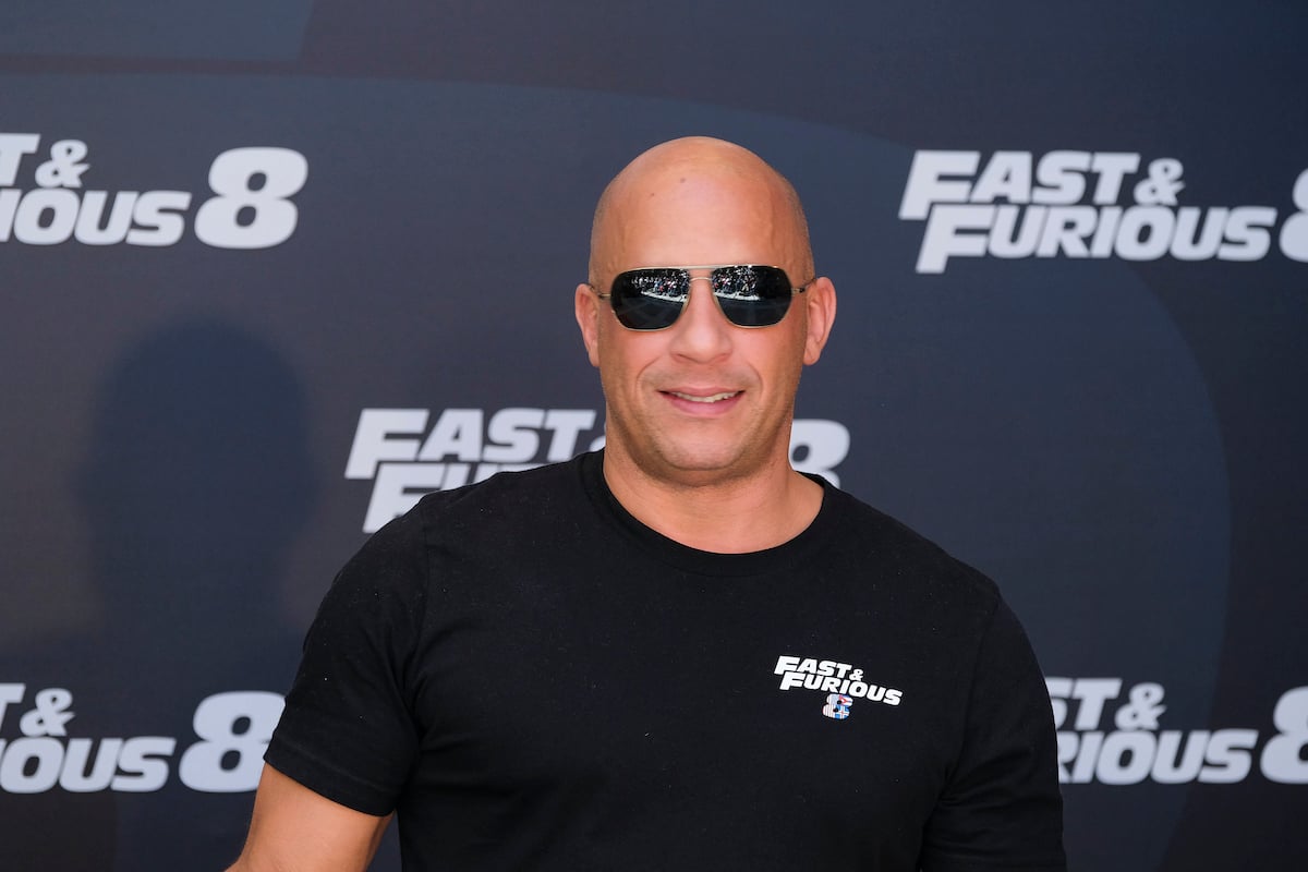 Vin Diesel wears sunglasses and smiles in front of the ‘Fast & Furious 8’ logo