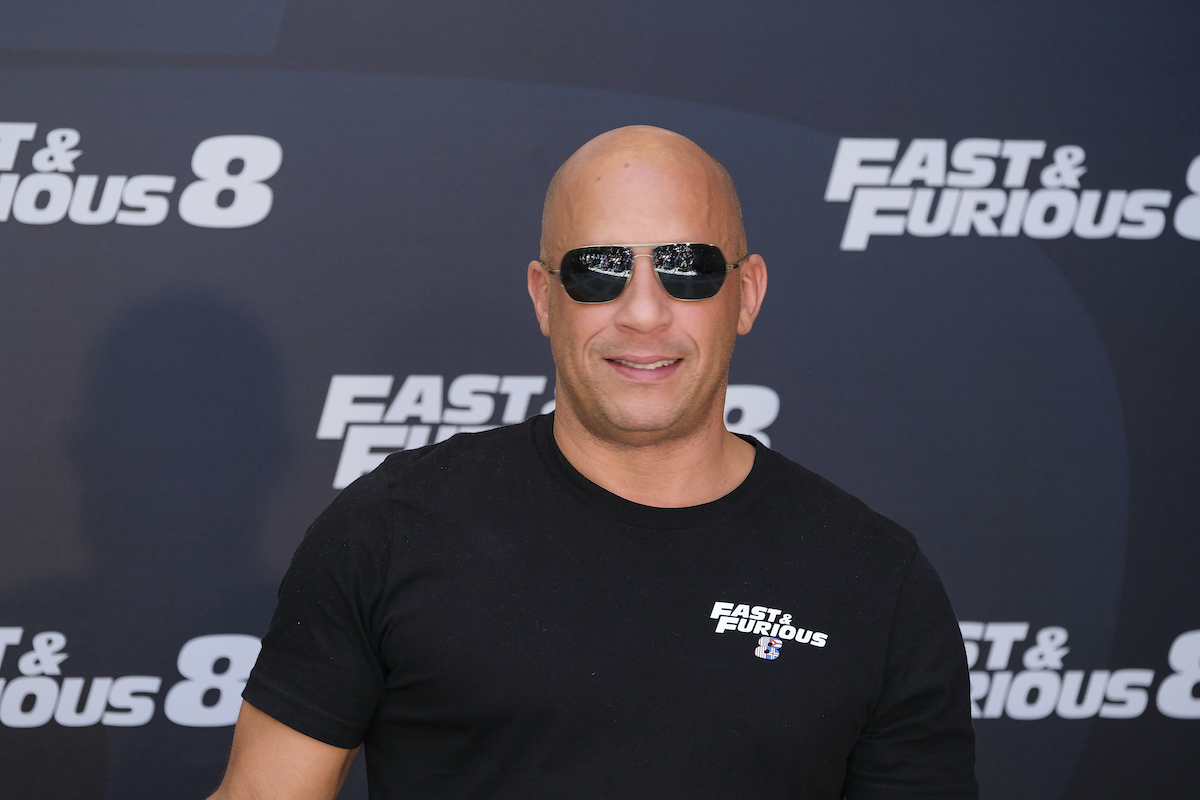 Vin Diesel wears sunglasses and smiles in front of the ‘Fast & Furious 8’ logo