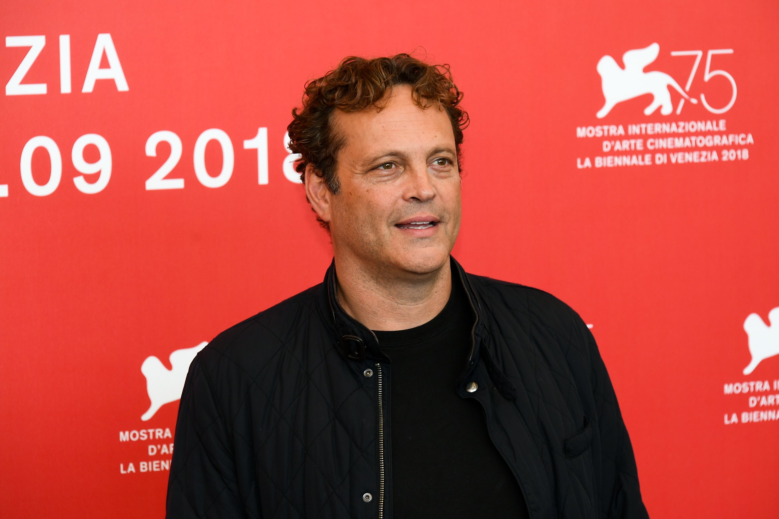 Vince Vaughn wearing a black jacket and standing in front of a pink wall