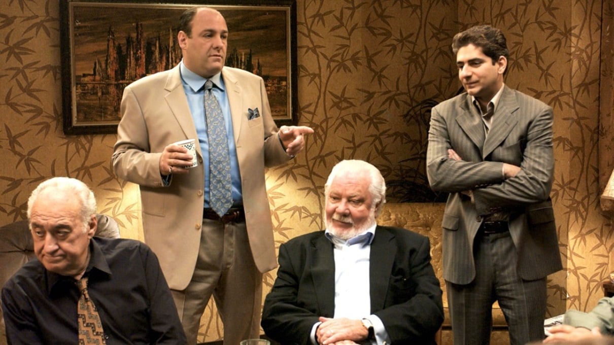 James Gandolfini points as Michael Imperioli looks while others sit around a card table in a 'Sopranos' episode.