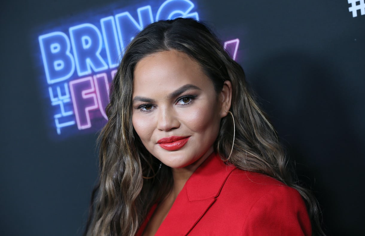 Chrissy Teigen smiling in red jacket