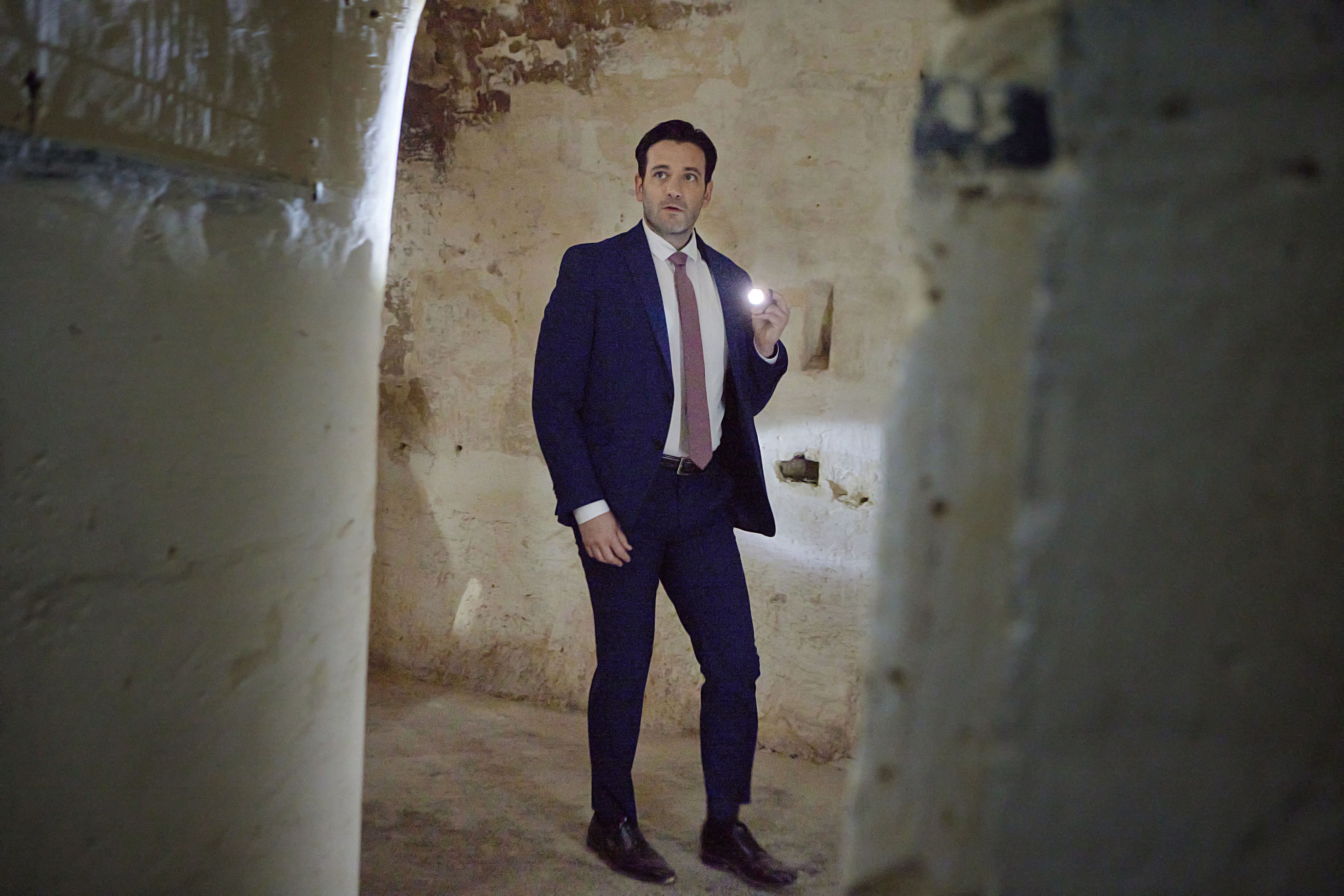Colin Donnell wearing a suit and holding a flashlight in 'To Catch a Spy'
