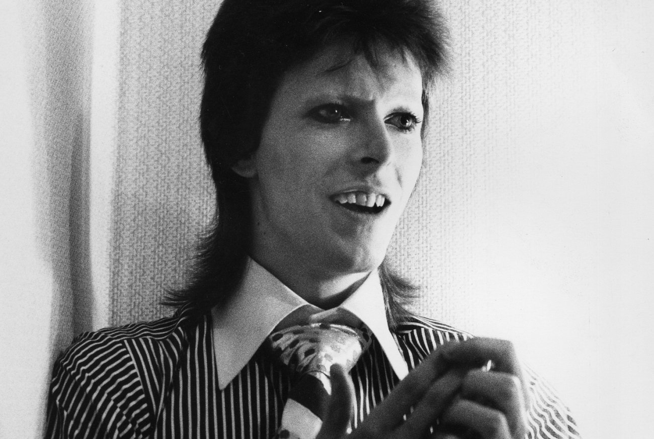David Bowie smiles an open-mouthed smile while holding his hands together in 1973.