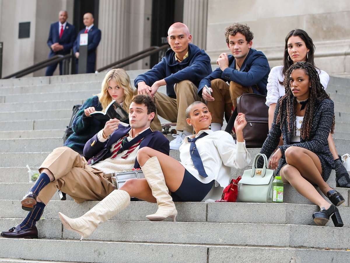 The cast of the 'Gossip Girl' reboot sitting together on stairs outside of a building