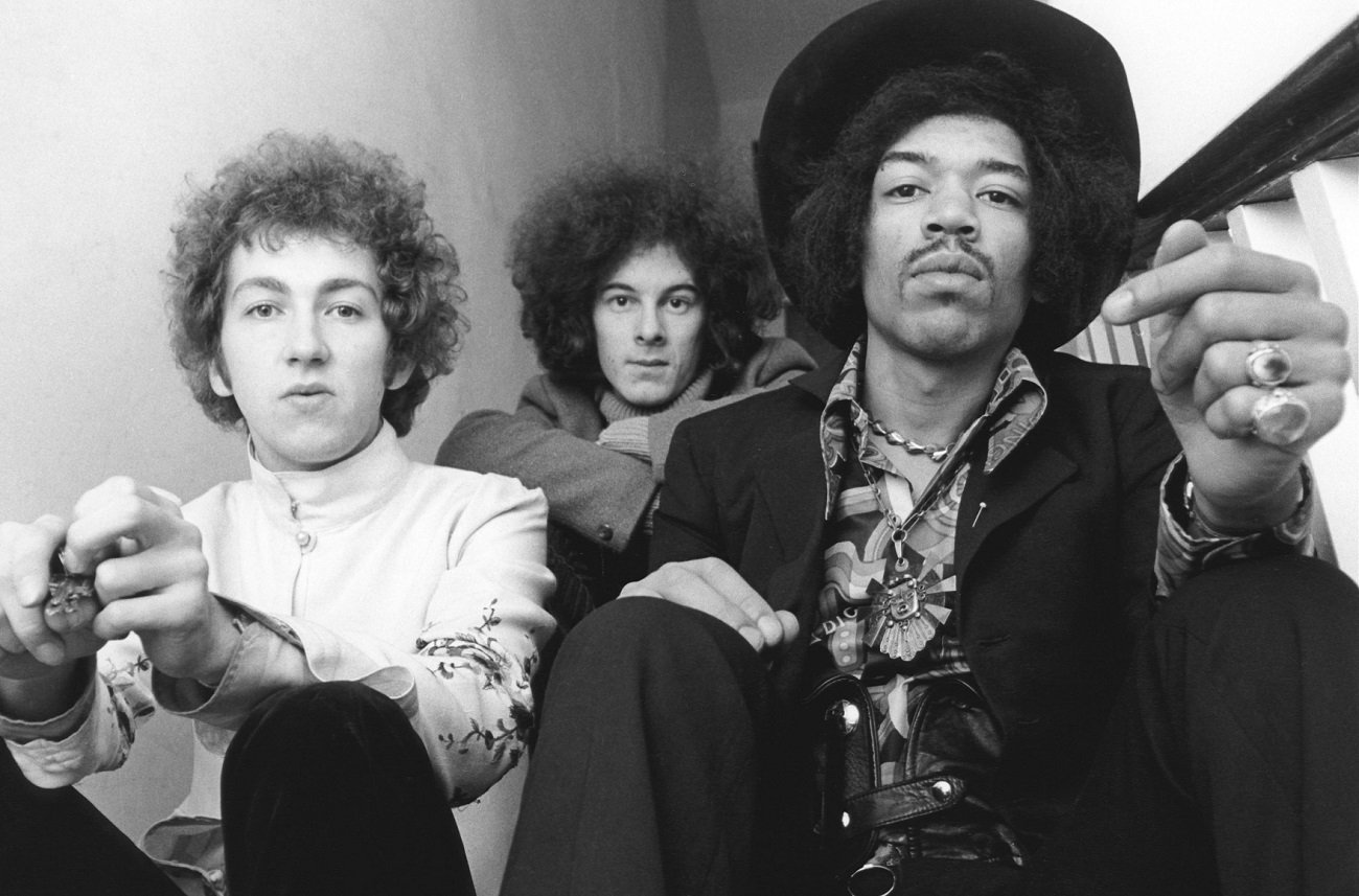 The 3 members of the Jimi Hendrix Experience pose for the camera while seated.