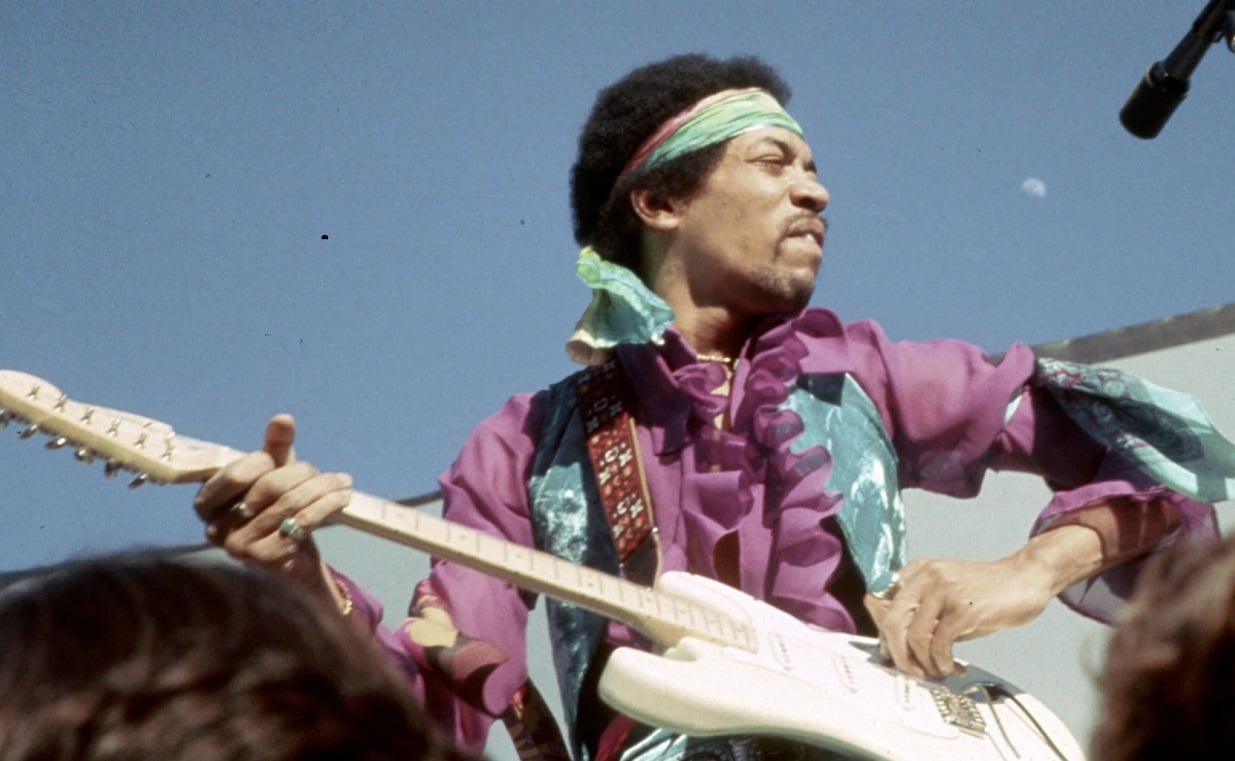 Close-up of Jimi Hendrix playing guitar on stage at an outdoor festival, 1969