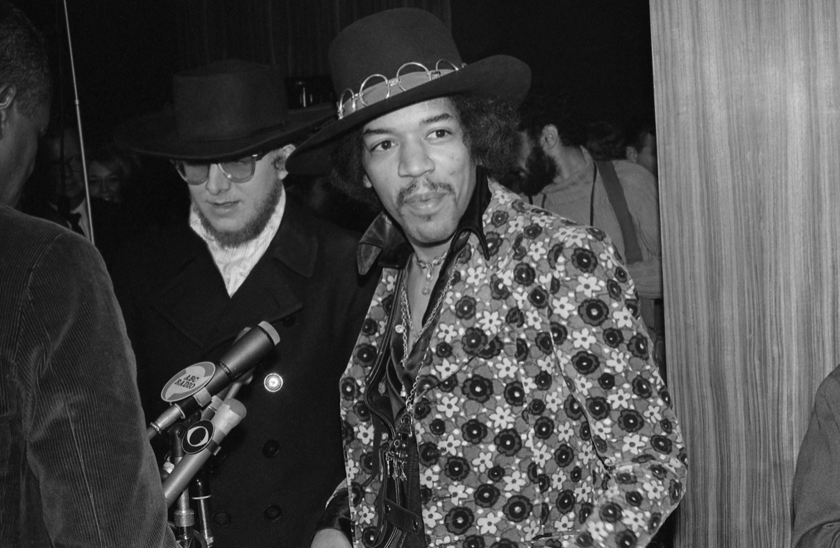 Jimi Hendrix grins while standing at a microphone and looking off camera in 1968.