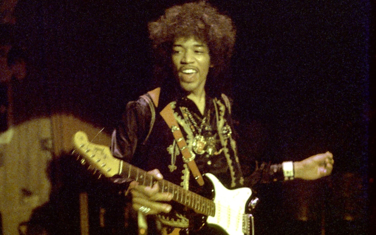 Jimi Hendrix smiles and plays guitar on stage in 1968.