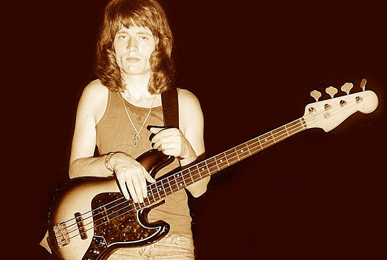 John Paul Jones stands staring at the camera with his bass guitar strapped on