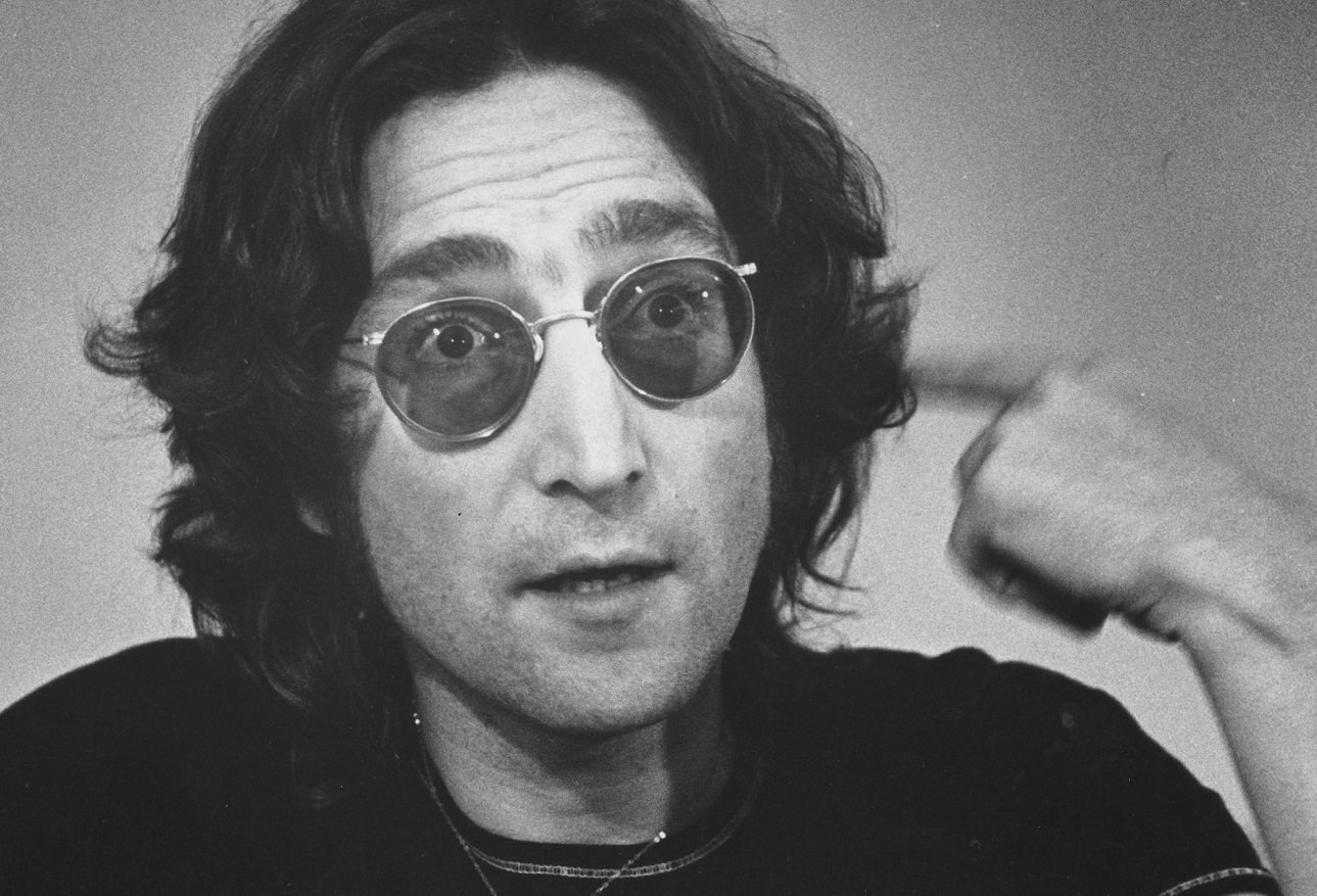 John Lennon, wearing sunglasses, points to his head during a '74 interview.