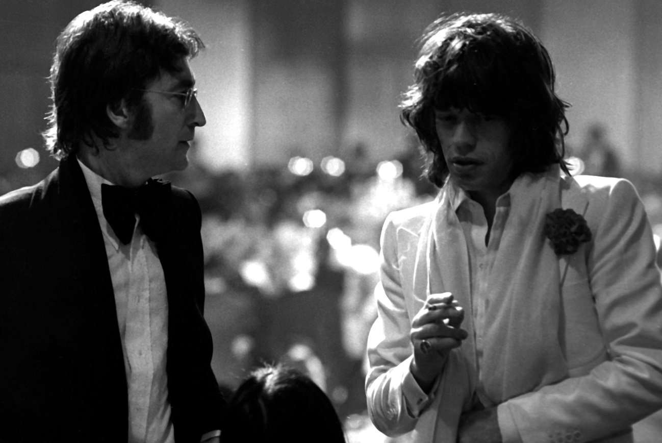 John Lennon looks at Mick Jagger, who's smoking a cigarette and looking away