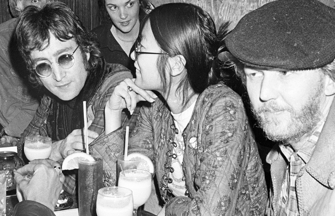 John Lennon sits in a club with May Pang and Harry Nilsson to his left in 1974.