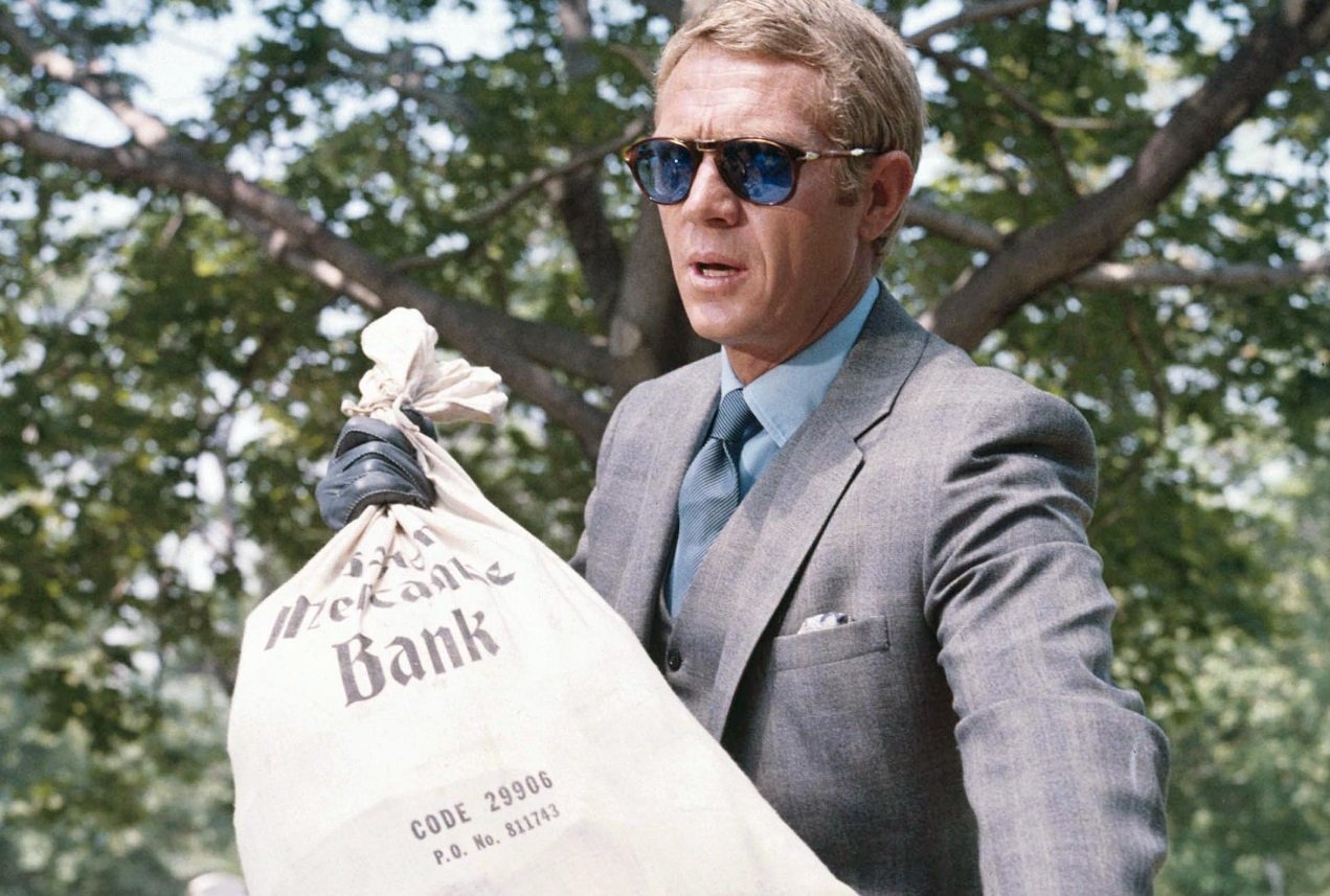 Steve McQueen, wearing sunglasses, retrieves a bag of stolen money from a waste bin in a publicity image issued for 'The Thomas Crown Affair,' 1968.