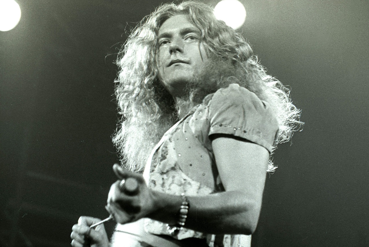 Robert Plant holds a microphone and gazes into the audience during a '70s performance.