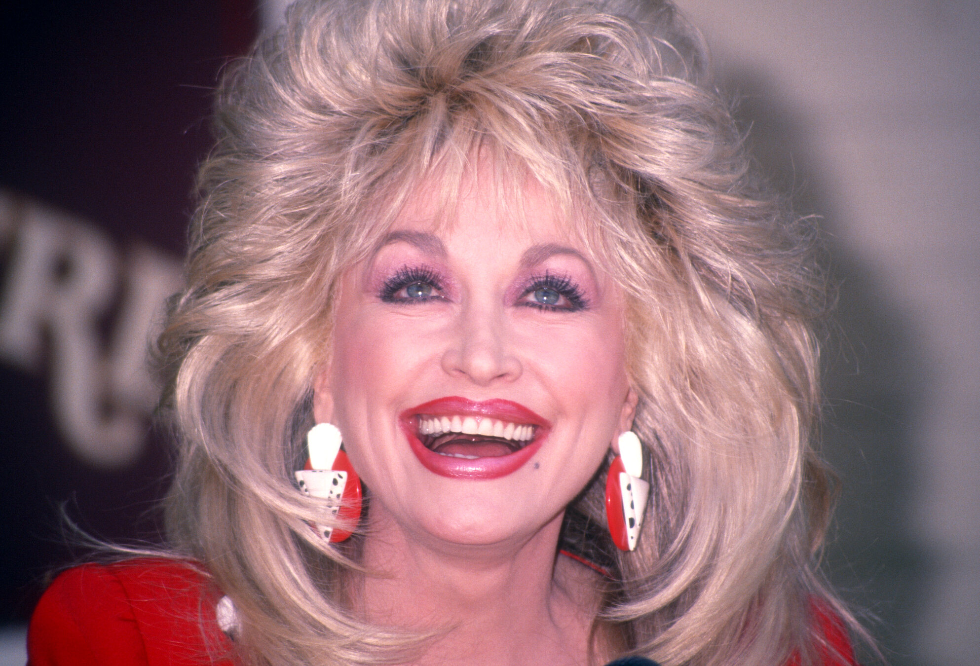 A close-up of Dolly Parton with her big, blonde hair, red lips, and red earrings.