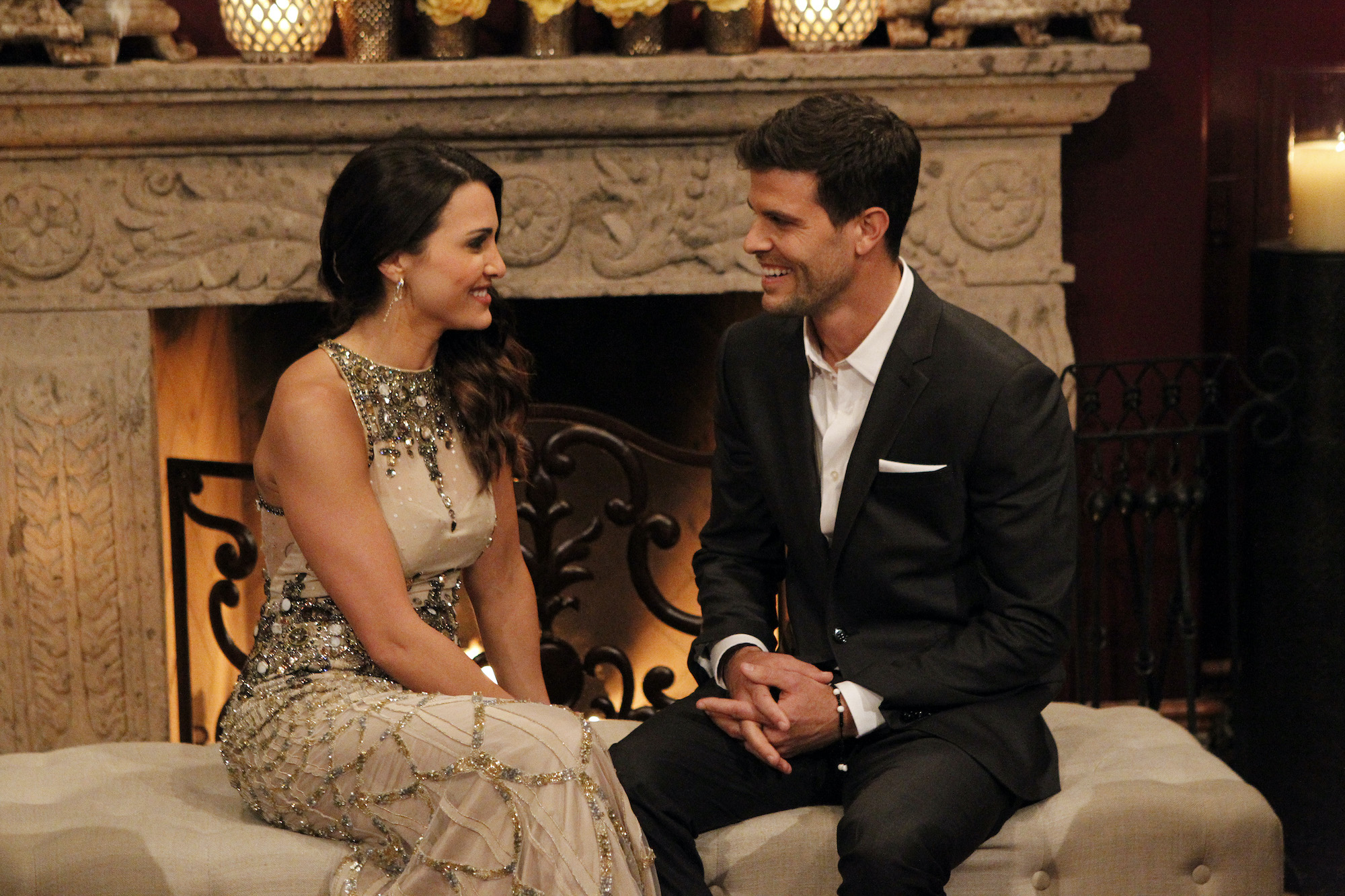 Andi Dorfman and Eric Hill smiling, seated in front of a fireplace